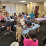 Instructor demonstrates massage techniques to a class in a training session.